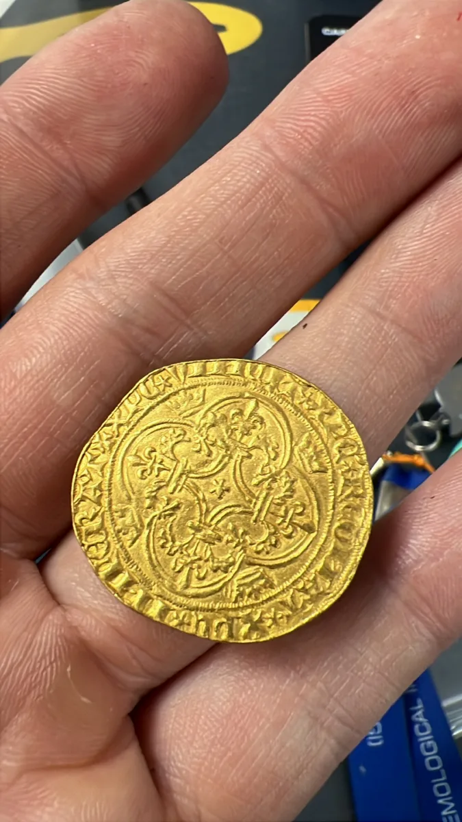 An ancient hammered gold coin held carefully for inspection