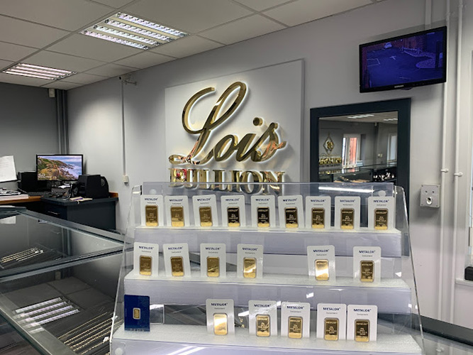 Metalor gold bars on a display shelf on the Lois Bullion showroom counter with the Lois Bullion logo on the wall.