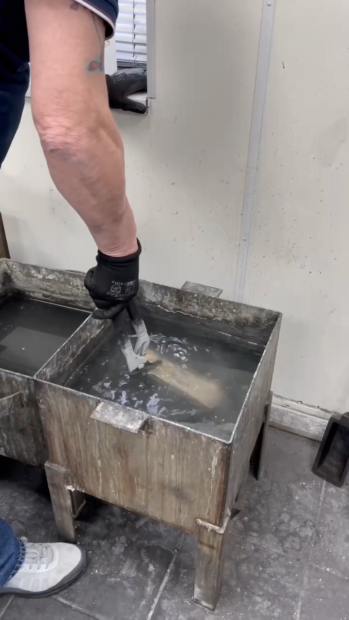 Submerging the gold bar into a water-filled bucket for cooling