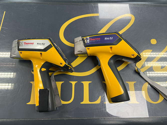 Two Thermo Scientific Niton XL2 handheld XRF guns on the Lois Bullion shop counter, used for precise metal analysis and valuations.